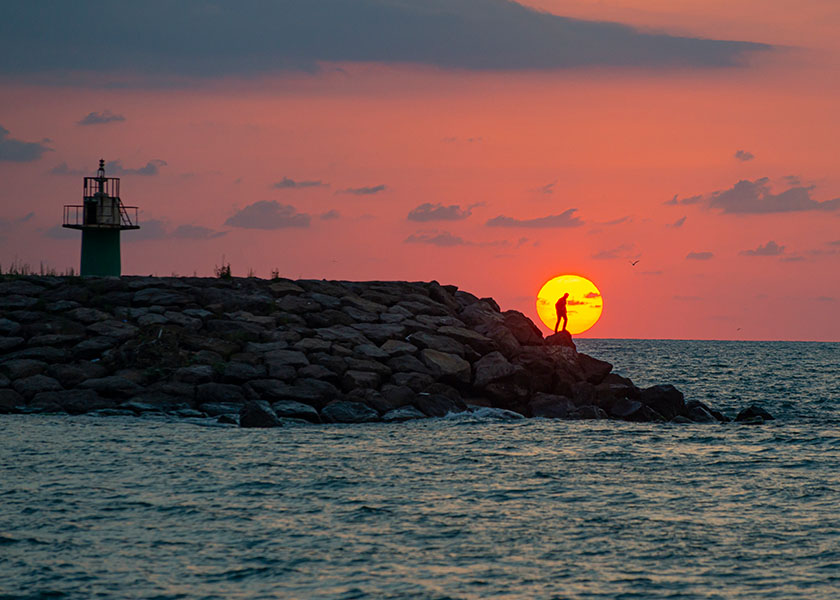 Man standing at lighthouse railing under sunset sky
